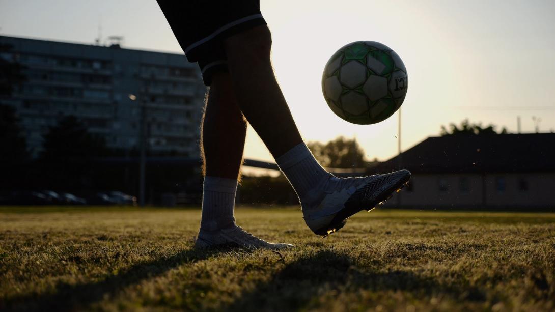 benen van jonge man die bal schopt op groen veld